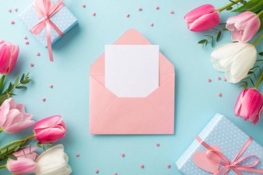 Anneler Günü konsepti. Açık pembe zarfın en üstteki fotoğrafı. Lale harfli. Mavi kutular. Kurdeleli kurdeleler ve izole edilmiş pastel arkaplan üzerine serpiştirmeler.