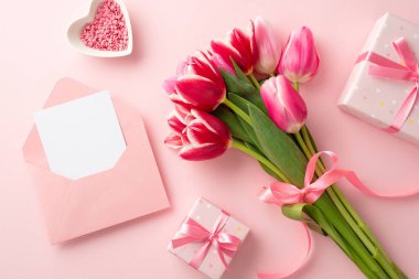 Anneler Günü konsepti. Kurdele hediye kutularıyla bağlanmış lale buketinin en üstteki fotoğrafı mektup ve kalp şeklinde fincan tabağıyla kaplı açık bir zarf ve kopyalanmış pastel pembe arka plan üzerine serpiştirilmiş.