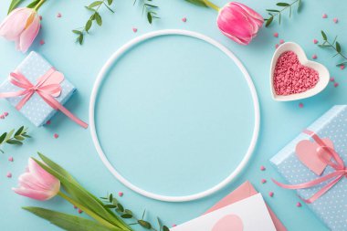 Anneler Günü konsepti. Boş yuvarlak çerçeve lalelerinin en üstteki fotoğrafı hediye kutuları zarf içinde harf ve kalp şeklinde fincan tabağı izole edilmiş pastel mavi arkaplan ve ortada telif alanı