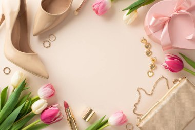 Üst düzey Anneler Günü hediye konsepti. Üstten görünümlü el çantası, lüks makyaj ürünleri, yüksek topuklu ayakkabılar ve ortasında telif alanı olan pastel bej bir arka planda çiçek aranjmanları.