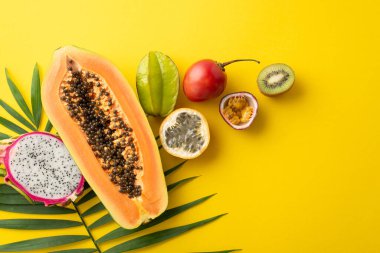 Yaz zevki konsepti. Taze ejderha meyvesi, papaya, çarkıfelek meyvesi, sarı arka planda yeşil palmiye yapraklı Carambola.