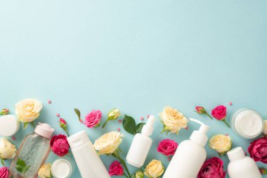 Gül esinlenilmiş cilt bakımı konsepti. Serum pompası şişesi ve krema şişesinin üst görüntüsü pastel mavi arka planda güzel gül çiçekleri ve boş bir alan