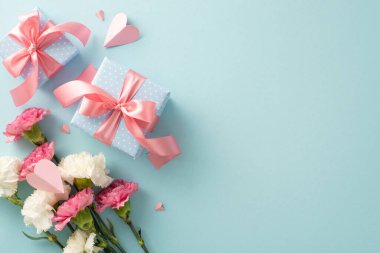 Anneler Günü konsepti. Üst görünüm düz fotoğraf pembe kurdeleli hediye kutuları, karanfil çiçekleri, ve pembe kağıt kalpler pastel mavi arka plan üzerinde boş alan metin veya reklam için
