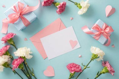 Anneler Günü mutluluk konsepti. Üstünde pembe kurdeleler, karanfil çiçekleri ve pastel mavi arka planda boş metin için boşluk olan pembe kağıt kalplerin olduğu boş kartpostal hediye kutularının en üstteki düz fotoğraf yatıyordu.
