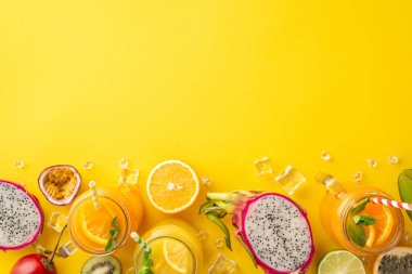 Meyveli bir vaha. Cam kavanozda renkli ve lezzetli meyve suyu veya kokteyl, ejderha meyvesi, kivi, portakal, kivi, limon, tutku meyvesi renkli, sarı arka planda boş alan.