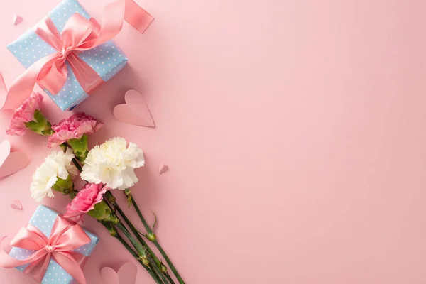 Mother's Day gift concept. Top view of elegant present boxes with pink ribbon, pretty carnation flowers, and cute paper hearts on a pastel pink background with space for text or branding