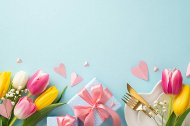 Anneler günü konsepti. Tabaklar, çatal bıçaklar, laleler, hediye kutuları ve pastel mavisi arka planda dekoratif kalplerin yer aldığı son moda masa dekorasyonu. Metin veya reklam için boş boşluk