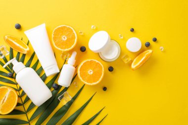 Parlak yaz teni konsepti. Üst kattaki düz tabaka krema şişeleri, kavanozlar, serum, sarı arka planda turuncu dilimler olan pipet.