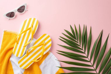 Yaz tatili konseptinin en iyi görüntüsü. Sarı çizgili terlikler, havlu, yeşil palmiye yaprakları, pastel pembe arka planda klasik güneş gözlükleri.
