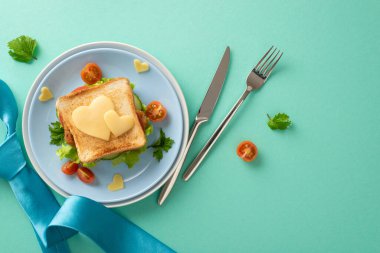 Babalar Günü kahvaltısı sürprizi ile babanın yüzüne bir gülücük getir. Sebzeli, kalp şeklinde peynirli, çatal bıçaklı, turkuaz arka planda mavi kravatlı ev yapımı bir sandviç.