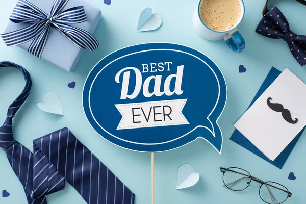 stock image Contemporary Father's Day design. Overhead view of greeting plaque, necktie, bow-tie, spectacles, paper hearts, giftbox, envelope with card, and coffee cup on pastel blue surface