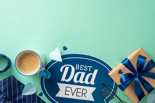 stock image Sophisticated Father's Day concept. Top view of greeting card, craft paper giftbox, necktie, hearts, accessories, glasses, coffee cup on teal background with empty space for advert