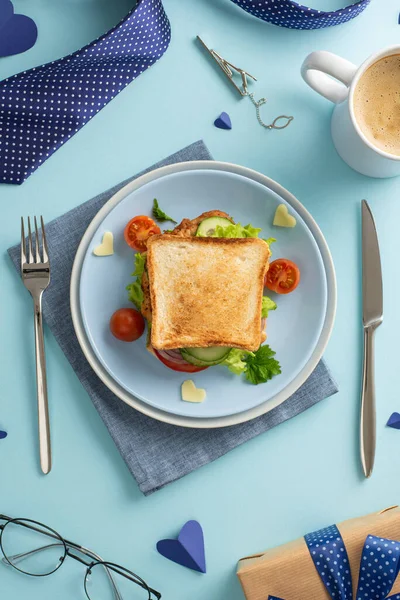 Babalar Günü 'nde ev yapımı kahvaltıyla babana sürpriz yap. Sebzeli sandviçin dikey resmi kahve, çatal bıçak takımı ve pastel mavi arka planda erkek aksesuarları.