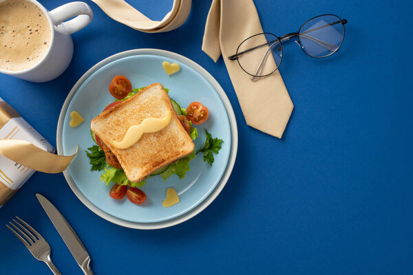 Celebrate Father's Day with a creative breakfast concept on blue background, including top view of plate, homemade sandwich with mustaches shape cheese, coffee, cutlery, giftbox, tie, and spectacles