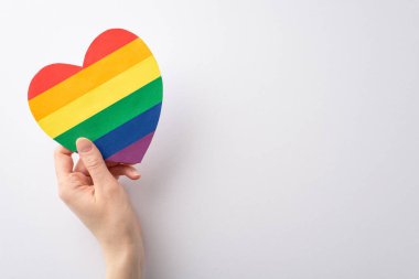 LGBTQ Tarih Ayı 'nı, beyaz bir arkaplanda yazı veya reklam için yeri olan kalp şeklinde gökkuşağı renkli bir kart tutan bir kadının üst görünüm fotoğrafı ile kutlayın