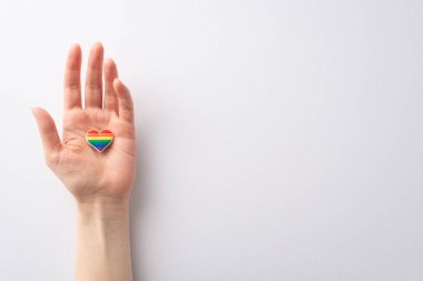 İlk bakışta, LGBTQ Tarihi Ayı anısına beyaz bir arkaplanda kalp şeklinde bir rozet taşıyan genç bir kadının eli.