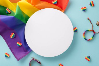 LGBT Tarih Ayının temel ihtiyaçlarının genel görünümü. Gökkuşağı bayrağı, rozetler, renkli kalp sembolleri, bileklik, metin veya reklamlar için boş bir daire ile mavi bir arkaplanda düzenlenmiş.