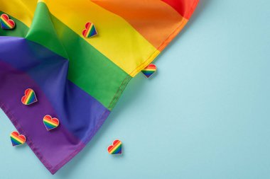 LGBTQ Tarih Ayı konsepti. Gökkuşağı temalı geçit aksesuarları, sembolik bayraklar ve pastel mavi arka planda boş metin veya reklam alanı olan rozetler üst görünüm düzlüğü