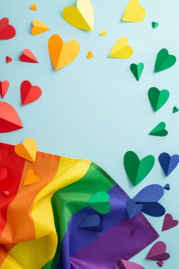Gökkuşağı bayrağı ve renkli kalpler de dahil olmak üzere, LGBTQ + geçit töreninin sahip olması gereken sembolik dikey düz yatağı, metin veya reklam için boş bir çerçeve ile pastel mavi bir arkaplan üzerine kuruludur.