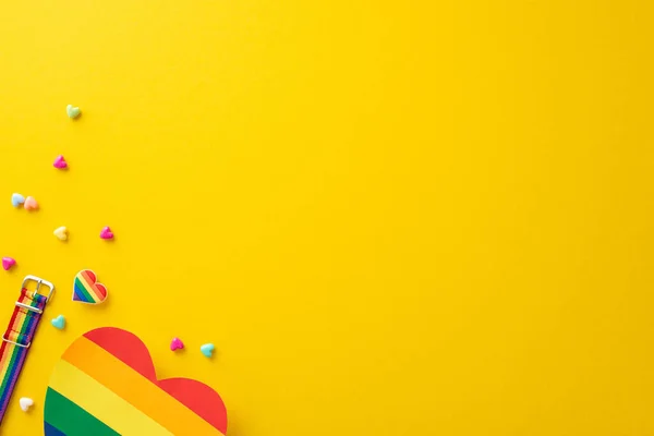 Stock image A top view flat lay of parade symbolic accessories, including wristlet, badge, hearts, rainbow card, on yellow backdrop with empty space for text or ad, celebrating the theme of Pride and inclusivity