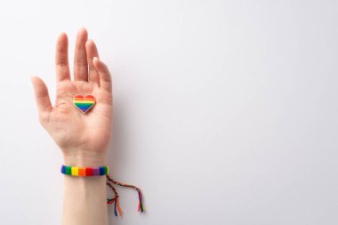 Gökkuşağı renkli bir bilezik takmış bir kadının beyaz arka planda LGBTQ Tarihi Ayı 'nı kutlayan, mesaj veya reklam için yeri olan kalp şeklinde bir rozet taşıyan ilk kişi fotoğrafı.