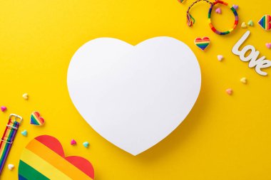 Bir dizi LGBT gurur geçidi aksesuarı, bir bilezik, rozetler, gökkuşağı renginde kalpler, üst bir görünüm düz uzanmış çarpıcı sarı bir zemin üzerine uzanmış metin veya reklam için boş bir daire ile