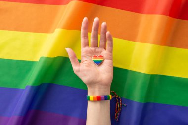 Genç bir kadının elinin gökkuşağı bileziği ve kalp şeklinde bir rozetle gökkuşağı bayrağı arkaplanına karşı çekilmiş bu ilk resmi reklam yapmak için mükemmel.