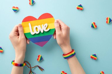 Bu ilham verici resimle LGBT topluluğuna desteğinizi gösterin. Mavi arka plandaki rozetlerin üzerine sembolik bir bilezik takan bir kadının elinde gökkuşağı kalp şeklinde bir kart.