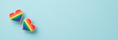 LGBTQ + destekleyici öğelerin yukarıdan çekimleri, gökkuşağı renklerinde kalp şeklinde rozetler de dahil. Kopyalamak için geniş alana sahip Pastel mavi arkaplan