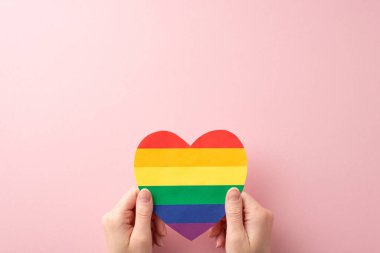 LGBT Tarih Ayı 'na katılın. Bu ilk kişi üstten bakıldığında gökkuşağı kalp şeklinde bir kartın kadın eliyle pastel pembe arka planda tutulduğu görüntüyü güçlendirir.