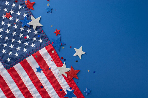 Memorial Day celebration concept. Overhead view of festive party decorations, including patriotic shimmering stars, confetti, American flag, set on blue background with space for text or advertisement