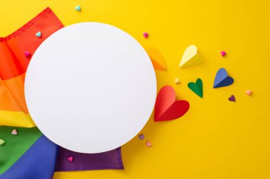 Sarı bir arkaplanda, gökkuşağı bayrağı ve kalpler gibi sembolik geçit aksesuarlarının üst görüntüsü, metin veya reklam için boş bir daire, birlik ve çeşitlilik teması onuruna