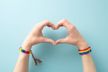LGBT destek fikri. Sembolik gökkuşağı bilezikleri takan kadınların birinci şahıs fotoğrafı. Mavi arka planda kalp jesti yaratıyor. Metin ya da reklam için geniş bir alanı var.