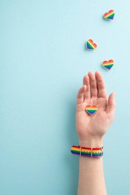 Elimin dikey fotoğrafında gökkuşağı bilekliği takıyorum ve mavi arka planda kalp rozeti taşıyorum. LGBT topluluğuna desteğimi gösteriyorum.