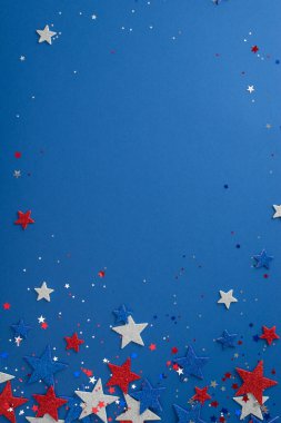 Bağımsızlık Günü için parti dekorasyonlarının dikey çekimleri. Parlayan yıldızlar ve Amerikan bayrağı renginde konfetiler mavi bir arkaplanda metin veya reklam için yer var