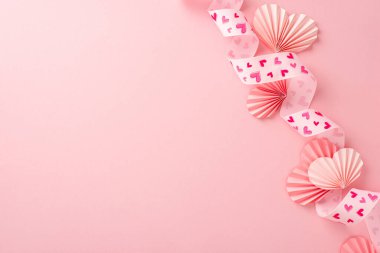 Pembe kurdeleli, basılı kalpler ve izole edilmiş pembe arkaplanlı kağıt origami kalpleriyle boş bir yerin üst görünüm fotoğrafı.