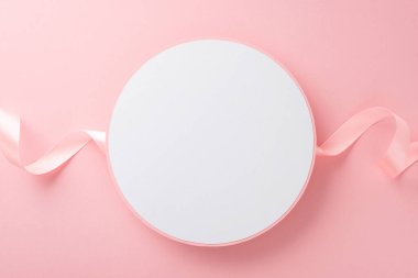 İzole edilmiş açık pembe arkaplanlı, pastel pembe kurdeleli boş beyaz dairenin üst görünüm fotoğrafı.