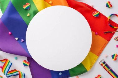 Bileklik, gökkuşağı bayrağı, kalp şeklindeki süsler ve rozetler gibi LGBT geçit aksesuarları beyaz bir yüzeye yerleştirilmiş, metin veya damgalama için boş bir daire ile işaretlenmiş.