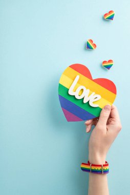 İlk bakışta, genç bir kadının elinin dikey bir fotoğrafı sembolik bir bileklikle LGBTQ + bayrak kartı taşıyor. Rozetlerin üzerinde mavi bir arka planda mavi renkli bir rozet ve kopyalanacak yer var.