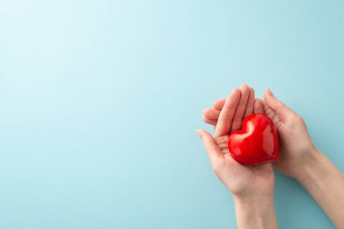 Kadın ellerinin pastel mavi arka planda kırmızı bir kalp sallarken çekilmiş ilk resmi. Mesaj ya da reklam için boş yer var. Dünya Kan Bağışı Günü konsepti.