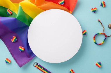 LGBT Tarih Ayı için bir dizi temel tören. Gökkuşağı bayrağının üst görüntüsü, rozetler, renkli kalpler, bilezik, mesaj veya metin için boş bir daire ile pastel mavi bir yüzeye serilmiş.