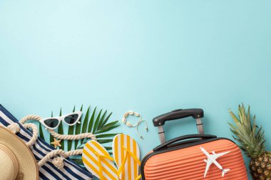 Yaz tatili titreşimleri! Bavulun üst görüntüsü, mini uçak biblosu, plaj aksesuarları, gözlükler, güneş şapkası, çanta, parmak arası terlikler, kabuk bileziği, ananas, palmiye yaprakları, açık mavi fon, reklam için boş alan.
