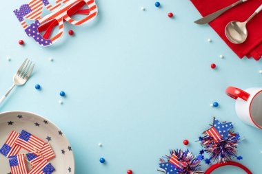 Bu masa düzeniyle Amerikan ruhunu göster. Üst manzara, tabak, fincan, çatal bıçak, peçete, saç bandı, gözlük, pastel mavisi arkaplanda ulusal bayrak. Metin veya tanıtım için çerçeve
