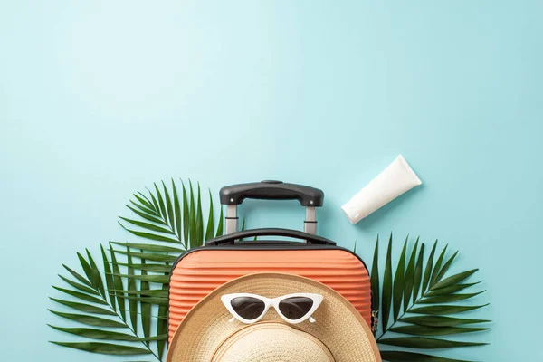 Stock image Dreamy holiday essentials. Orange suitcase seen from top view, beach essentials, stylish sunglasses, hat, sunscreen bottle and palm leaves on a pastel blue background, perfect for text or advertising