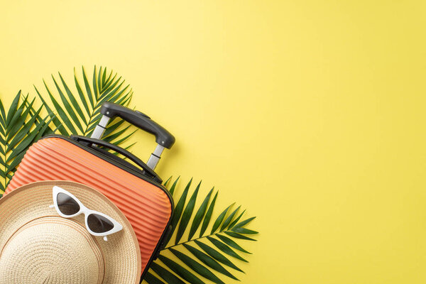Tropical travel essentials. Overhead shot of a vibrant orange suitcase, beach gear, eyeglasses, straw hat, and palm fronds against a yellow backdrop, perfect for text or advertising