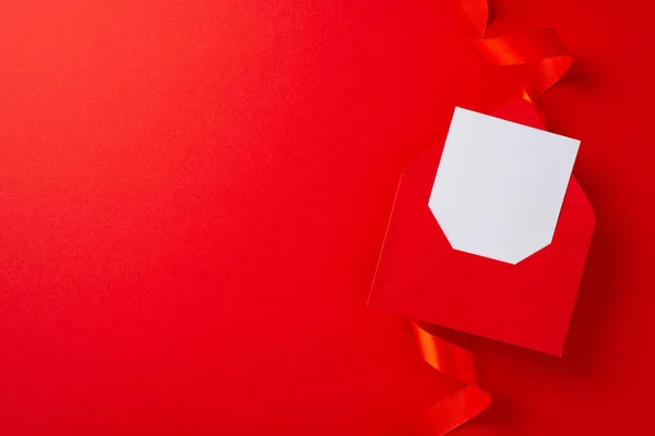 stock image Top view photo of white empty envelope surrounded by bright red ribbon and paper origami hearts on isolated red background with copy-space