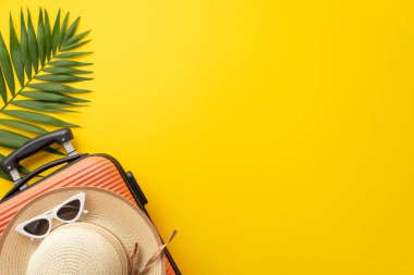 Yaz tatili ilhamı. Üst görünümde bavul, plaj ekipmanı, güneş gözlüğü, güneş şapkası ve yeşil palmiye yaprağı, çarpıcı sarı bir zemin var. Metin veya tanıtım içeriği için mükemmel