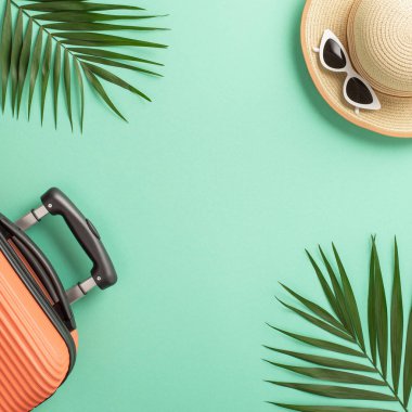 Yaz tatili kavramı. Üzerinde turuncu bir bavul ve saman şapka beyaz güneş gözlüğü ve kopyalanmış deniz mavisi arkaplanlı palmiye yaprakları var.