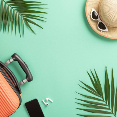 Yaz gezisi konsepti. Üzerinde turuncu bavul ve hasır şapkalı, güneş gözlüğü ve palmiye yapraklı, kopyalanmış turkuaz arka planda bir fotoğraf var.