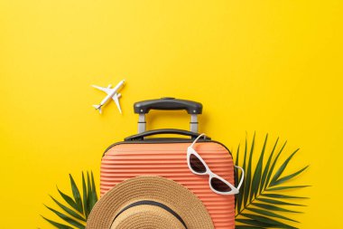 Yaz tatili kavramı. Üstünde güneş gözlüğü ve güneş gözlüğü olan turuncu bavul resmi. Palmiye yaprakları ve izole edilmiş, sarı arka planda, kopyalanmış bir uçak modeli.